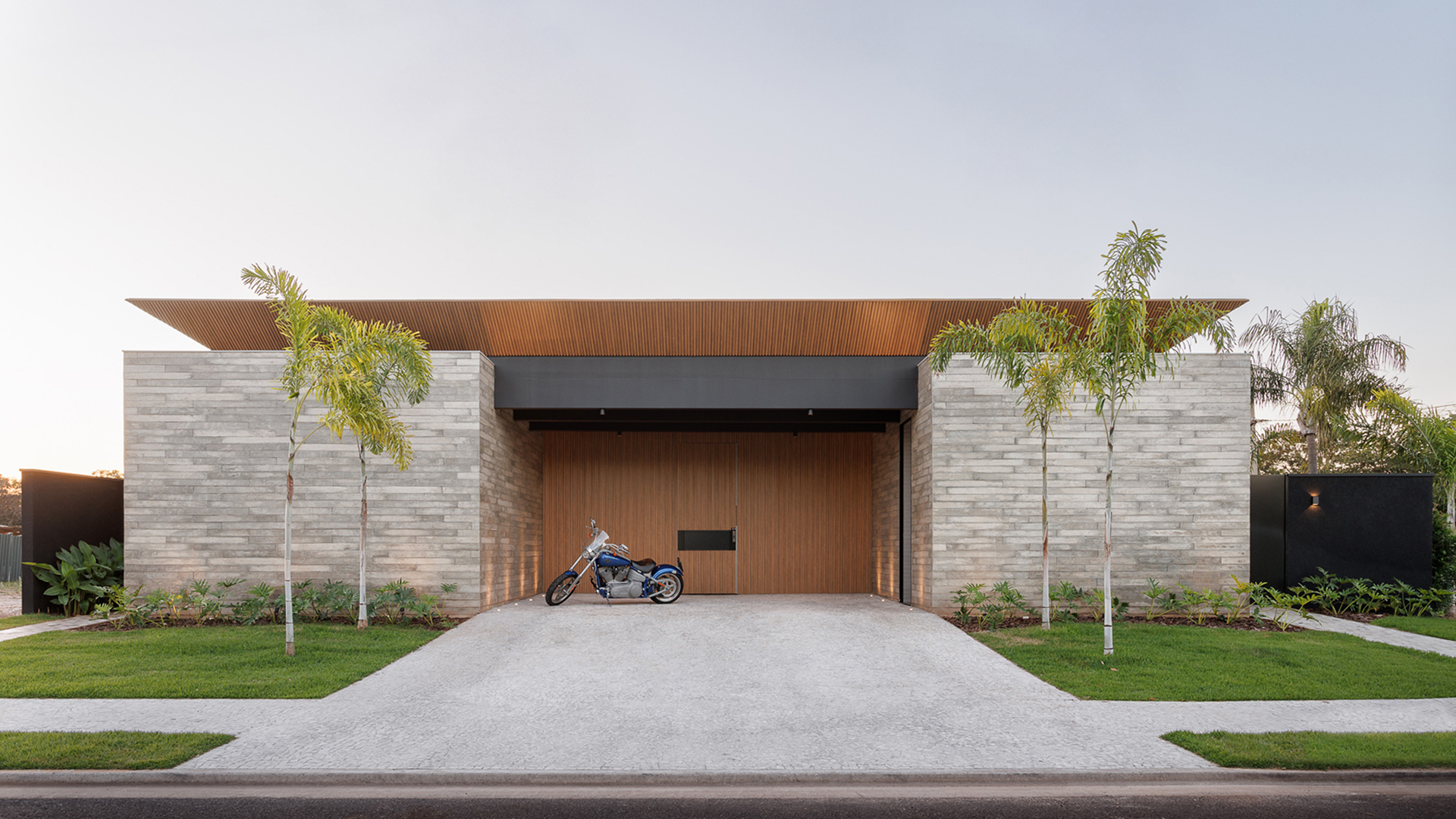 Casa minimalista moderna com paredes de concreto, detalhes em madeira e palmeiras na entrada